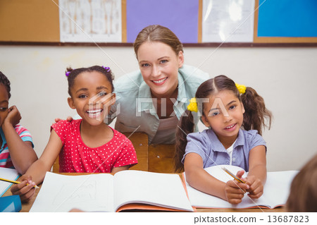 Cute pupils and teacher smiling at camera in classroom 13687823