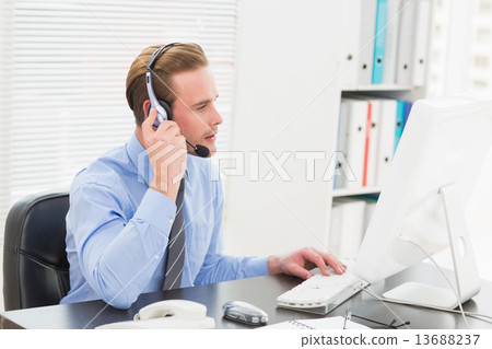 Businessman typing at computer while speaking with headset 13688237