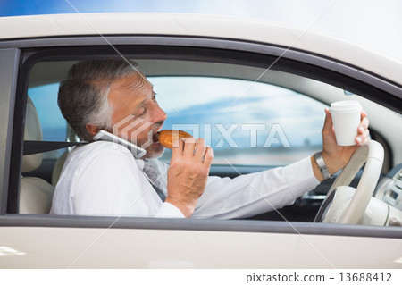 Man drinking coffee and eating donnut on phone 13688412