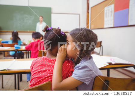 Cute pupils whispering in classroom 13688537