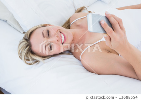 Smiling blonde woman lying in bed text messaging Smiling blonde woman lying in bed text messaging 13688554