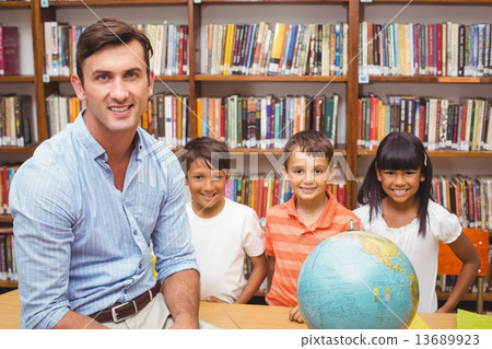 Cute pupils and teacher looking at globe in library Cute pupils and teacher looking at globe in library 13689923