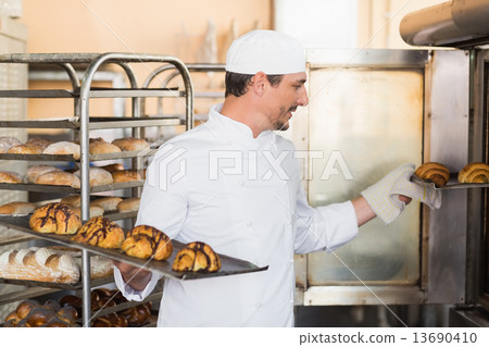 Smiling baker holding trays of croissants Smiling baker holding trays of croissants 13690410