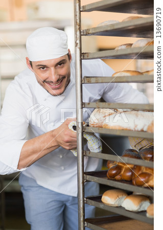 Smiling baker pushing tray of bread 13690719