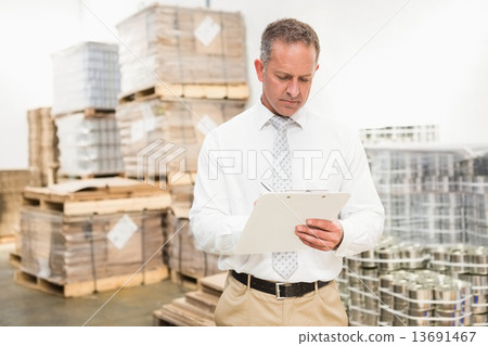 Warehouse manager writing on clipboard Warehouse manager writing on clipboard 13691467