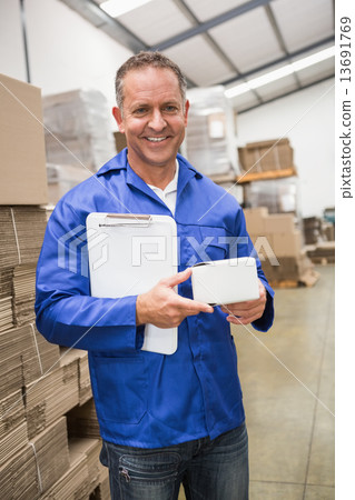 Smiling warehouse worker holding small box and clipboard 13691769