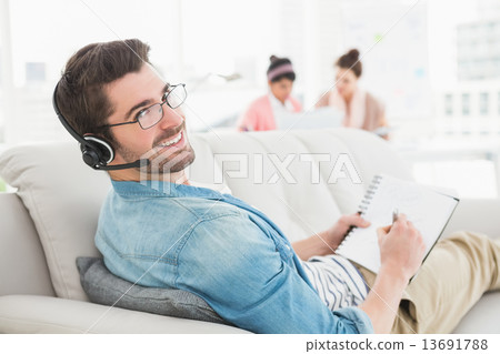 Smiling businessman phoning and taking notes on sofa 13691788