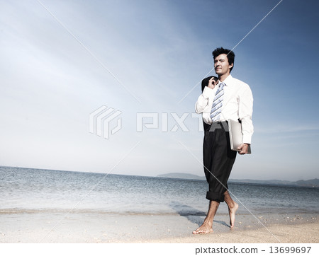 Businessman walking along a beach with laptop 13699697
