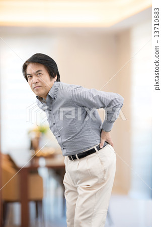Middle-aged man in casual wear suffering from back pain at home living Middle-aged man in casual wear suffering from back pain at home living 13710883