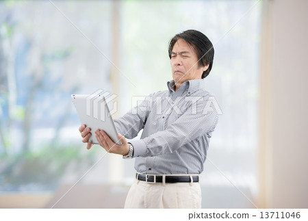 一個穿著休閒服的中年男子在家居客廳的窗戶操縱平板電腦 13711046