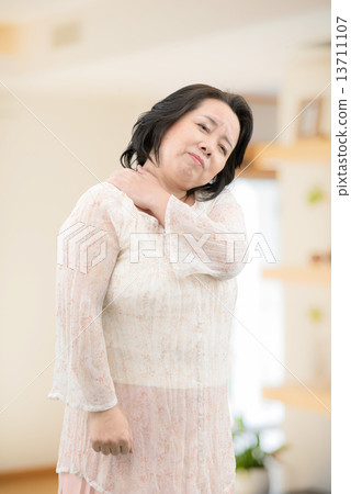 A middle-aged woman in casual wear suffering from low back pain, stiff shoulder standing in the room 13711107