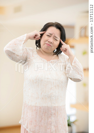 一名中年婦女穿著休閒服，患有腰痛，僵硬的肩膀站在房間裡 13711112