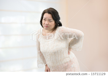 一名中年婦女穿著休閒服，患有腰痛，僵硬的肩膀站在房間裡 13711129