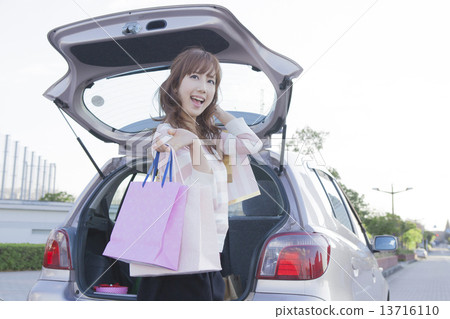 A woman with a shopping bag, opening the trunk of the car 13716110