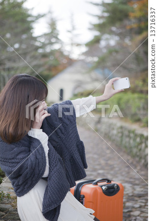 A smiling woman taking a picture by placing a trunk in the autumn cobblestone 13716337