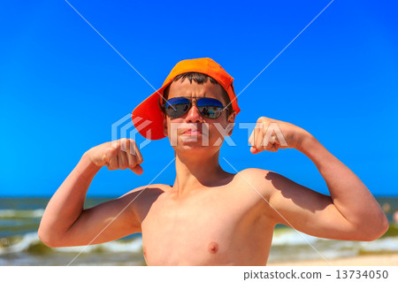 Happy young boy on the sea beach demonstrates biceps Happy young boy on the sea beach demonstrates biceps 13734050
