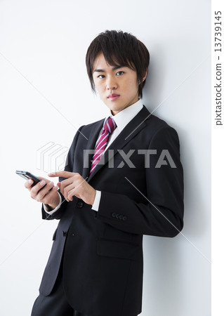 A young man in a suit manipulating a smartphone 13739145