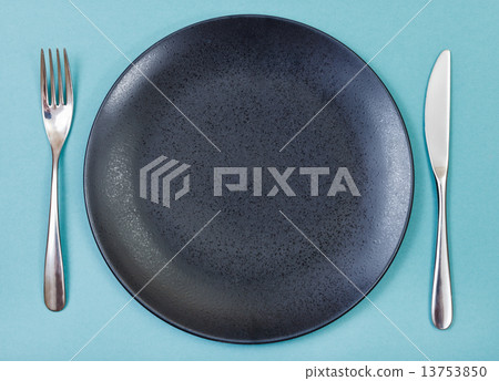 top view of black plate, fork, knife set on green 13753850