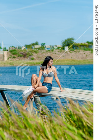 Young beautiful girl on the pier at the river with white hat in denim shorts 13761440