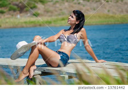 Young beautiful girl on the pier at the river with white hat in denim shorts 13761442