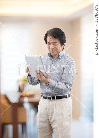 Middle-aged man in casual wear manipulating tablet at home living 13766975