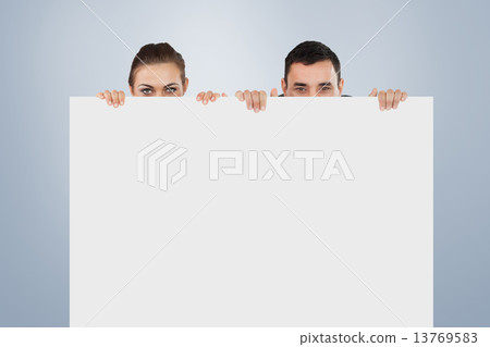 Composite image of business partners hiding behind a sign Composite image of business partners hiding behind a sign 13769583
