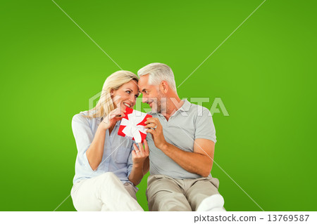 Composite image of happy couple sitting and holding present 13769587