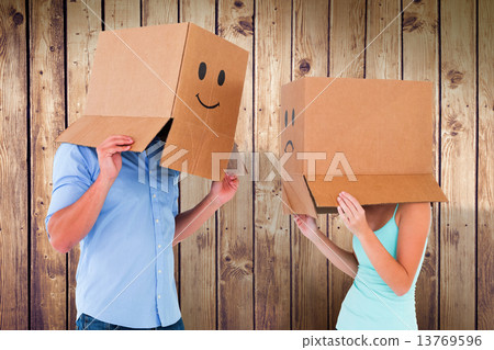 Composite image of couple wearing emoticon face boxes on their h Composite image of couple wearing emoticon face boxes on their h 13769596