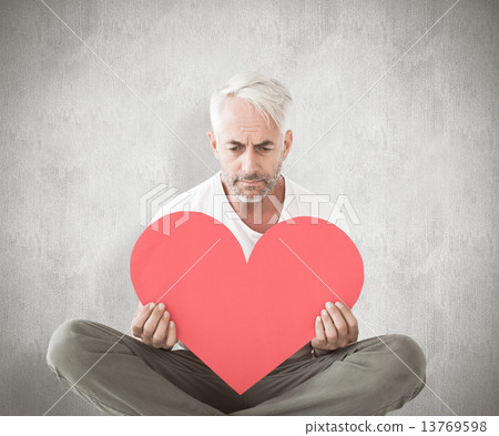 Composite image of upset man sitting holding heart shape Composite image of upset man sitting holding heart shape 13769598