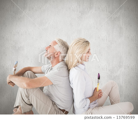 Composite image of happy couple sitting and holding paintbrushes Composite image of happy couple sitting and holding paintbrushes 13769599