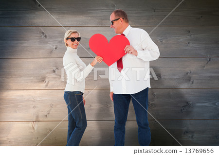 Composite image of older affectionate couple holding red heart s 13769656