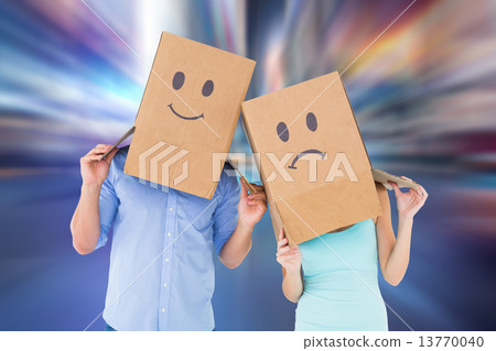 Composite image of couple wearing sad face boxes on their heads 13770040