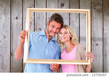 Composite image of attractive young couple holding picture frame 13770507