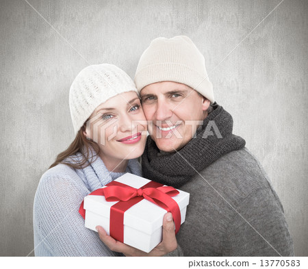 Composite image of casual couple in warm clothing holding gift Composite image of casual couple in warm clothing holding gift 13770583