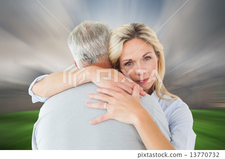 Composite image of unhappy blonde hugging her husband Composite image of unhappy blonde hugging her husband 13770732