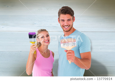 Composite image of young couple smiling and holding paintbrushes Composite image of young couple smiling and holding paintbrushes 13770914