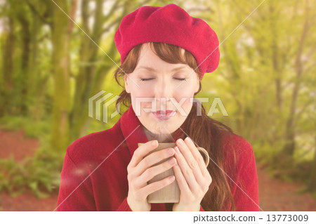 Composite image of woman holding a warm cup 13773009