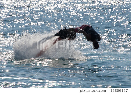 Flyboarder diving forwards headfirst into backlit sea 13806127