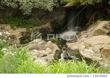 Blurred waterfall underneath trees in rocky landscape Blurred waterfall underneath trees in rocky landscape 13810993