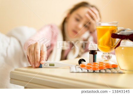 portrait of sick girl lying in bed and taking thermometer from t 13843145