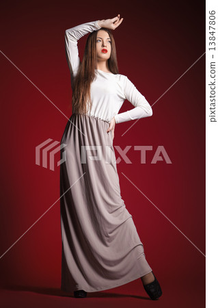 beautiful girl in long dress posing against red 13847806