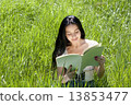 Photo of young attractive brunette woman sitting on grass and re 13853477