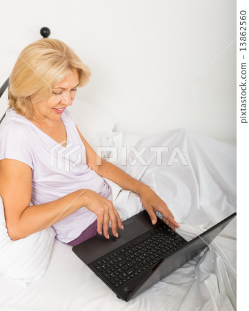 Mature woman with laptop in bed 13862560