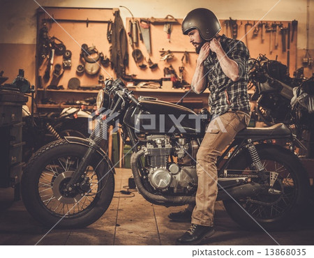 Rider and his vintage style cafe-racer motorcycle in customs garage 13868035