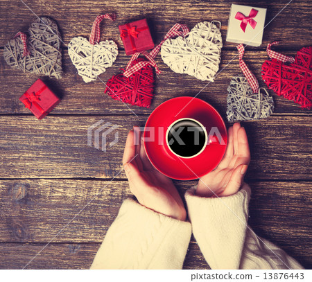 Female holding cup of coffee near heart shape toys on a table. Female holding cup of coffee near heart shape toys on a table. 13876443
