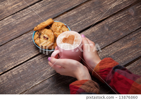 Female hands holding cup of coffee and cookies on wooden table. Female hands holding cup of coffee and cookies on wooden table. 13876860