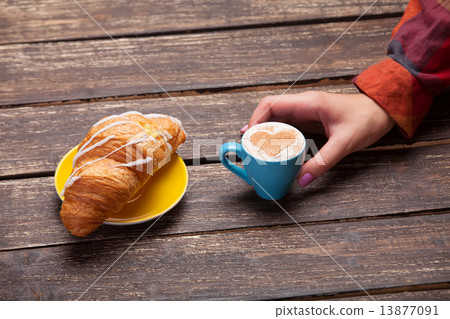 Female hands holding cup of coffee with croissant on wooden tabl Female hands holding cup of coffee with croissant on wooden tabl 13877091