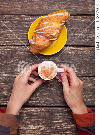 Female hands with cup of coffee and croissant on wooden table. Female hands with cup of coffee and croissant on wooden table. 13877408
