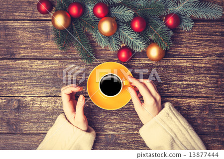 Female holding cup of coffee near pine brach on a table. Female holding cup of coffee near pine brach on a table. 13877444