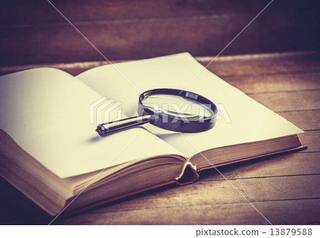 Loupa and book on wooden table 13879588